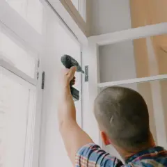 Mężczyzna przykręca zawias w oknie. Szybka wymiana okna to klucz do komfortu.