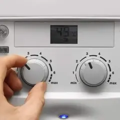 Ręka kręci pokrętłem pieca gazowego dwufunkcyjnego, ustawiając temperaturę. Wyświetlacz pokazuje 49°C.
