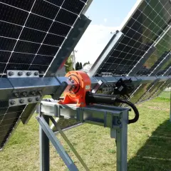 Mechanizm tracker pv z pomarańczową przekładnią i siłownikiem, obracający panele słoneczne na metalowej konstrukcji.