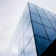 Nowoczesny budynek z geometrycznymi, błękitnymi szybami fotowoltaicznymi odbijającymi niebo.