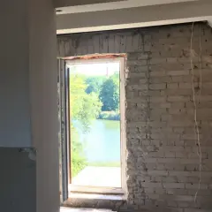 Trwa wymiana okien w domu z widokiem na jezioro. Widać surowe ściany i piankę montażową.