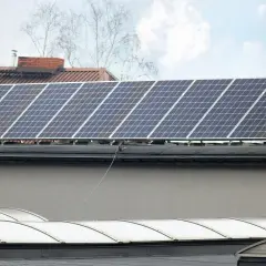 Panele fotowoltaiczne na dachu, gotowe do podgrzewania i produkcji energii. W tle budynki i drzewa.