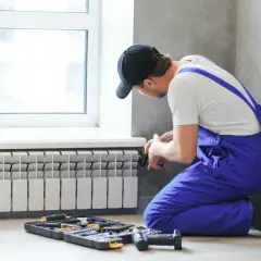 Instalator wykonuje podłączenie grzejnika od dołu. Obok leżą narzędzia.
