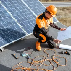 Przed odbiorem instalacji fotowoltaicznej pracownik w pomarańczowym stroju sprawdza projekt.