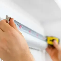Dłonie mierzą taśmą zwijaną szerokość okna typowego. Precyzja jest kluczowa przy montażu.