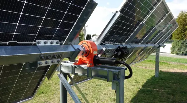 Mechanizm tracker pv z pomarańczową przekładnią i siłownikiem, obracający panele słoneczne na metalowej konstrukcji.