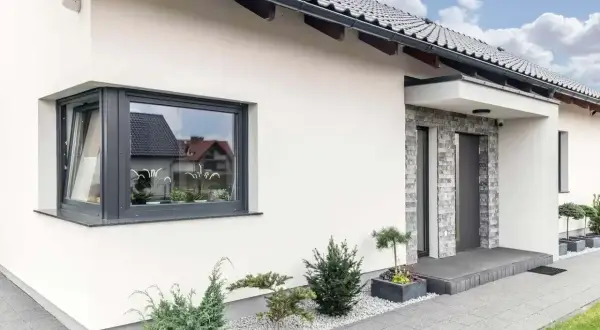 Nowoczesny dom z szarym, narożnym oknem ze słupkiem, kamienną elewacją przy drzwiach i zadbanym ogrodem.