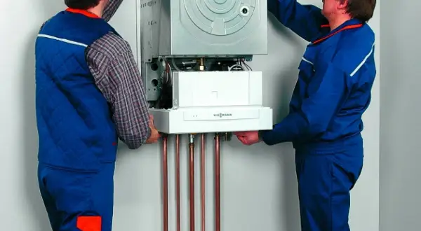 Dwóch techników montuje kocioł gazowy, zapewniając jego zabezpieczenie pieca gazowego przed przepięciem.