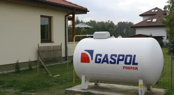 Biały zbiornik na gaz propan z logo GASPOL obok domu, zapewniający ogrzewanie gazem LPG.