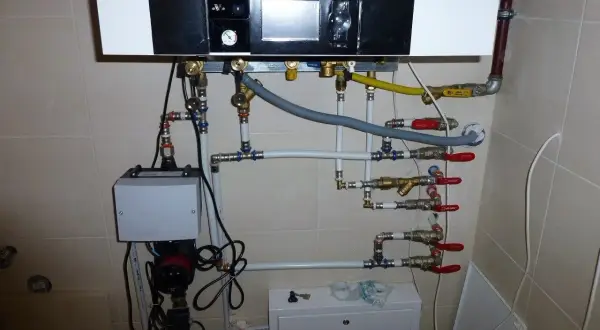 Podłączenie pieca gazowego kondensacyjnego. Widoczny panel sterowania, pompa, zawory i rury tworzące skomplikowaną instalację grzewczą.