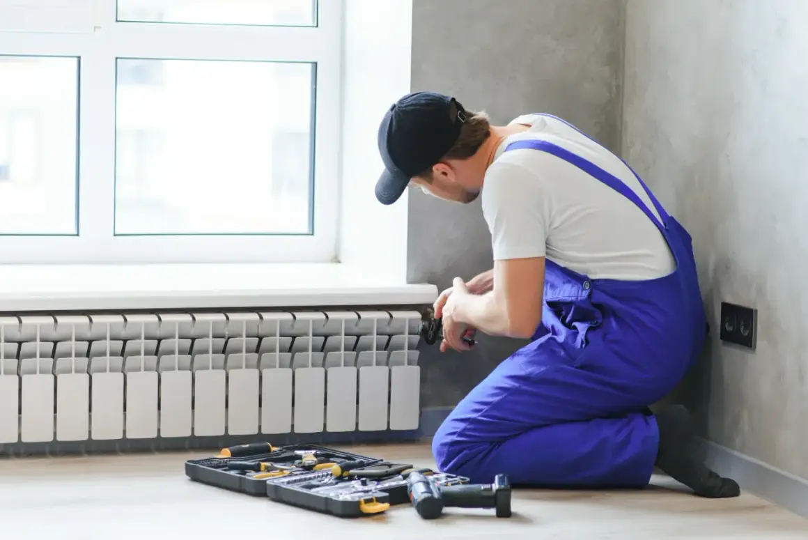 Instalator wykonuje podłączenie grzejnika od dołu. Obok leżą narzędzia.