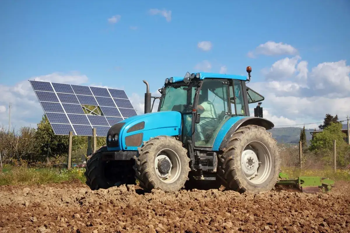 Błękitny traktor orze pole, a w tle panele słoneczne symbolizują energię dla wsi.