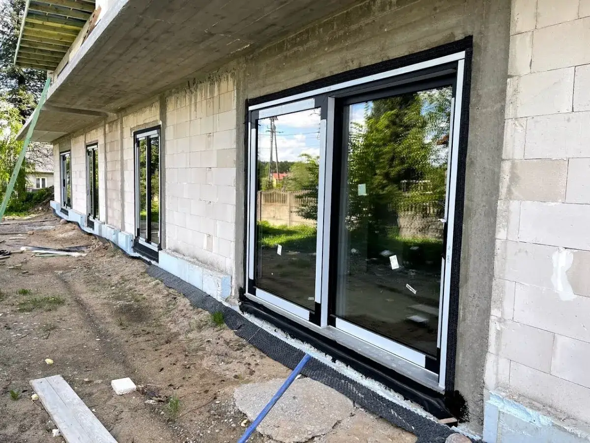 Fartuch EPDM montaż okien w nowym domu. Widok na budynek z białej cegły, z dużymi, czarnymi oknami.