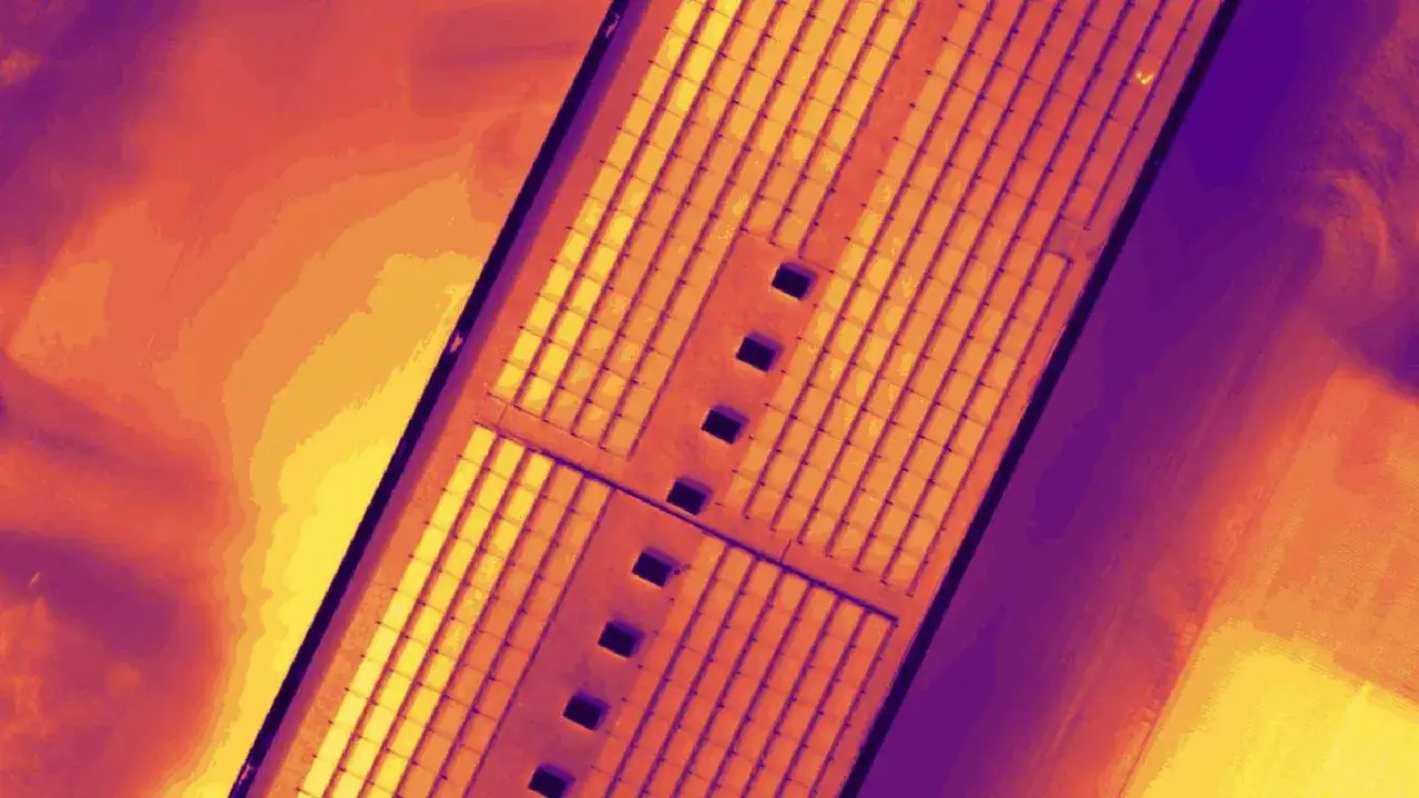 Termowizyjne ujęcie farmy fotowoltaicznej z widocznymi uszkodzeniami paneli. Ciepłe barwy wskazują na anomalie termiczne.