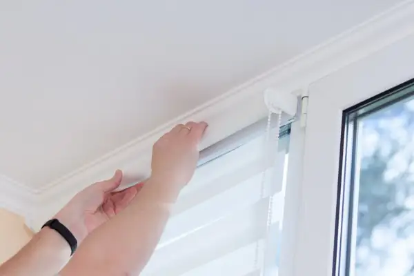 Ręce montują nową tkaninę w rolecie dzień noc, dopasowując ją do mechanizmu.